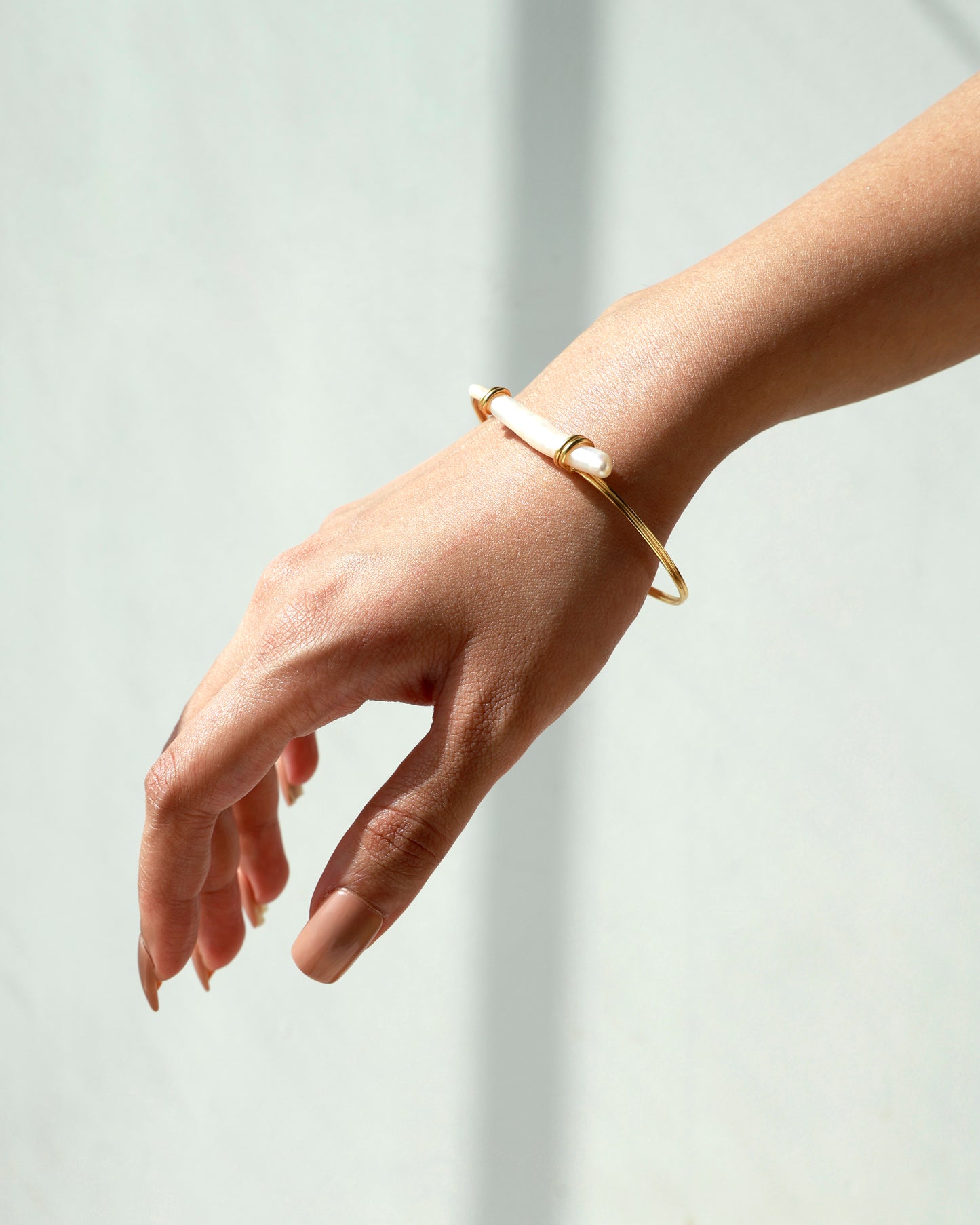 Gold bracelet on a person's wrist against a light background