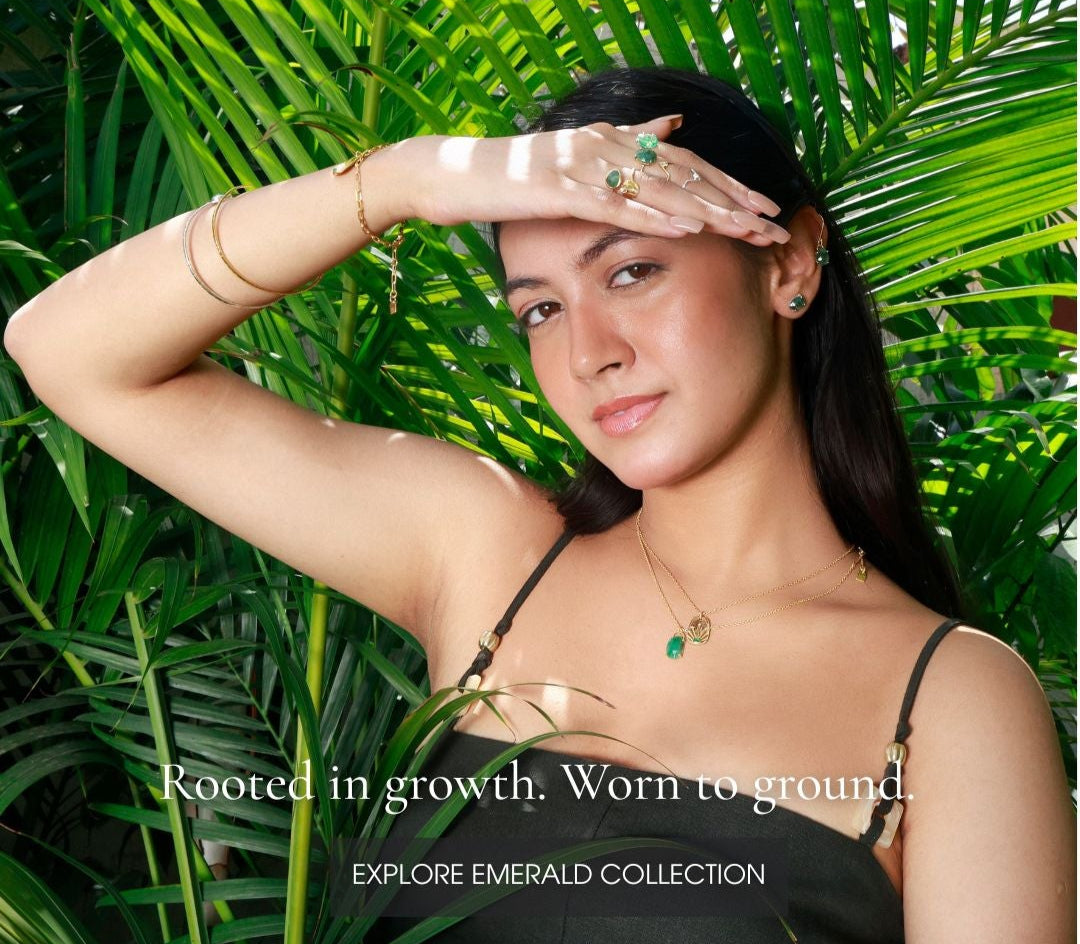 Woman with jewelry against a green leafy background, promoting the Emerald Collection.